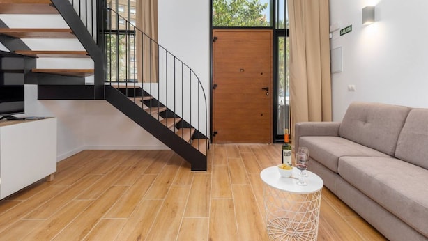 A modern living room with a wooden staircase, a sofa, a coffee table, and a door labeled "SALIDA". - Alameda suites loft 1. (Valencia / València)