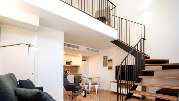 A modern apartment with a living area, kitchen, dining space, and a staircase.