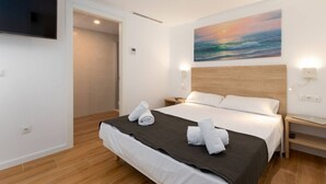 A hotel room with a bed, a painting, a TV, and a wooden floor.
