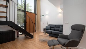 A modern interior with a staircase, a grey sofa, a grey armchair, and a round coffee table.