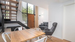 A modern interior with a wooden table, white chairs, a grey sofa, and a staircase.
