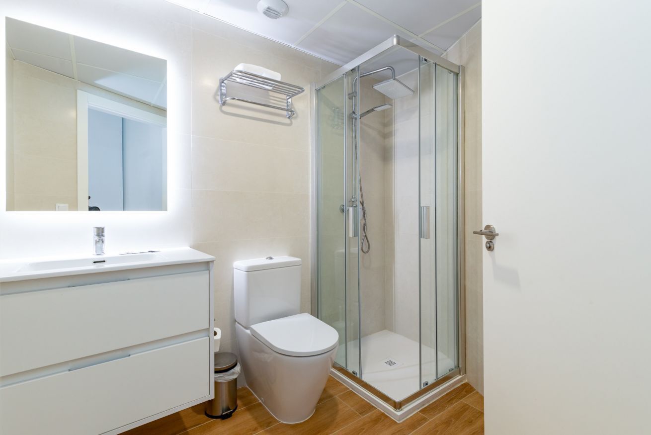 A modern bathroom with a glass-enclosed shower, a white sink with a mirror, and a toilet.