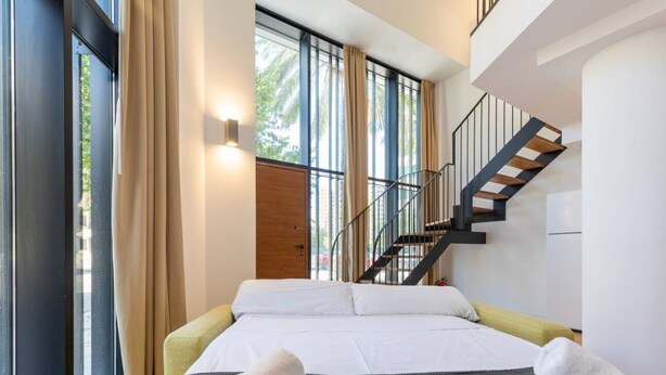Een moderne hotelkamer met een groot bed, een trap en grote ramen.