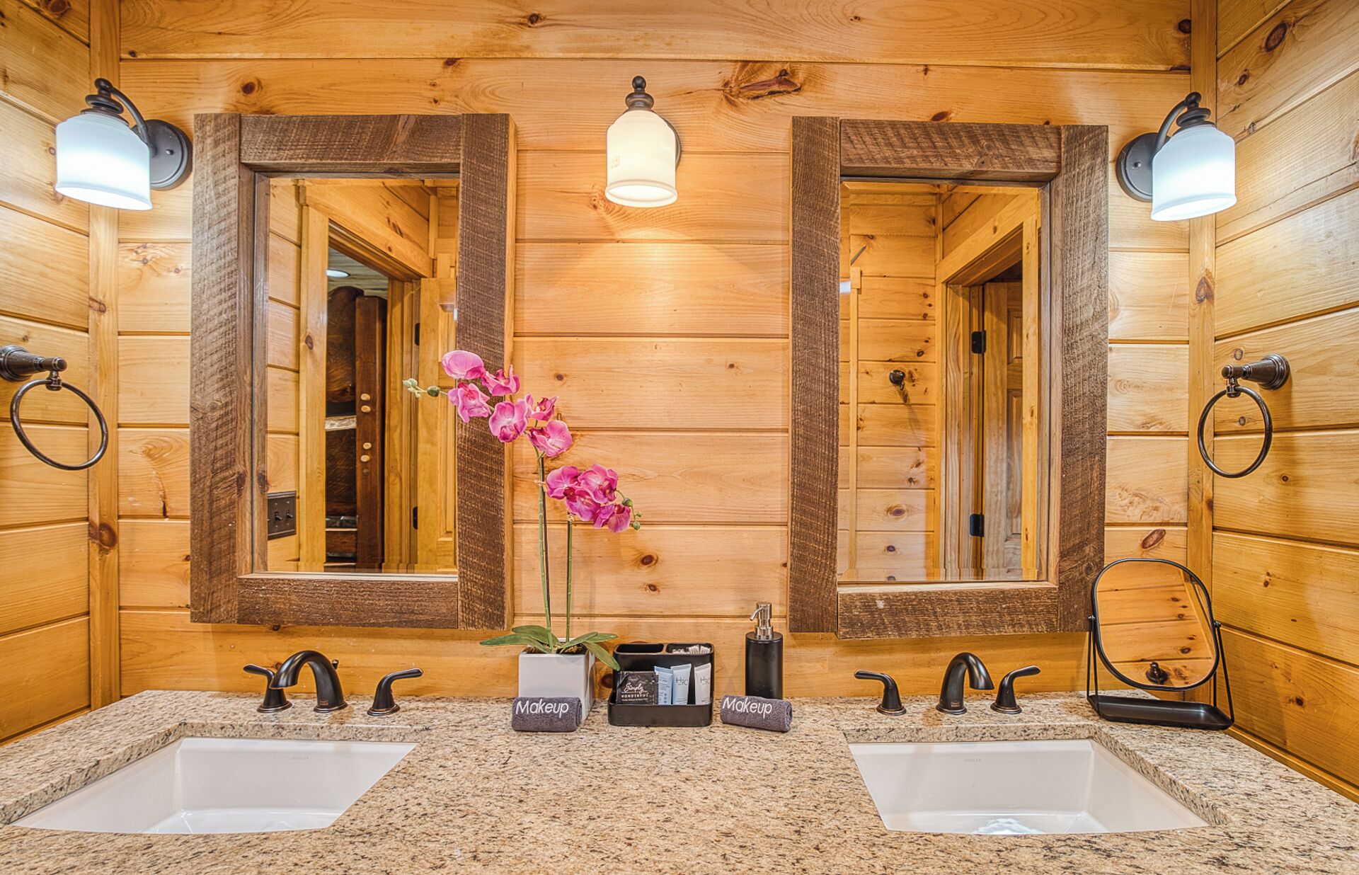 Une salle de bain rustique, avec des murs en bois, comprenant deux lavabos, un miroir et une orchidée en pot.