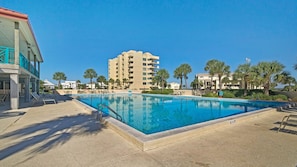 Piscina com Ɣgua azul cristalina, rodeada por espreguiƧadeiras e palmeiras.