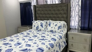 Ein Schlafzimmer mit Bett, Nachttischen, einem Schminktisch und einem Fenster mit Vorhängen.