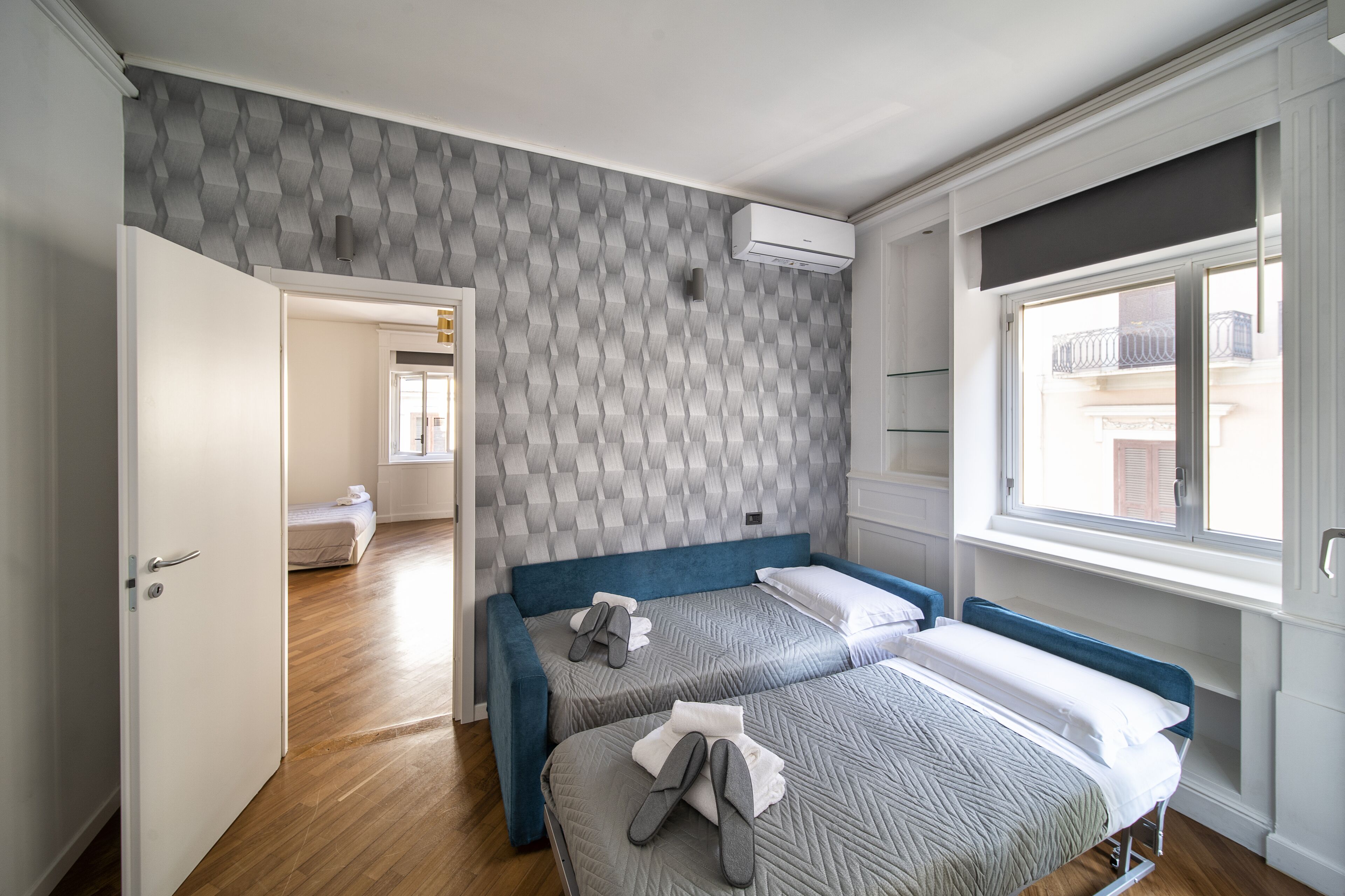 A bedroom with two beds, a patterned wall, and a window with a view.