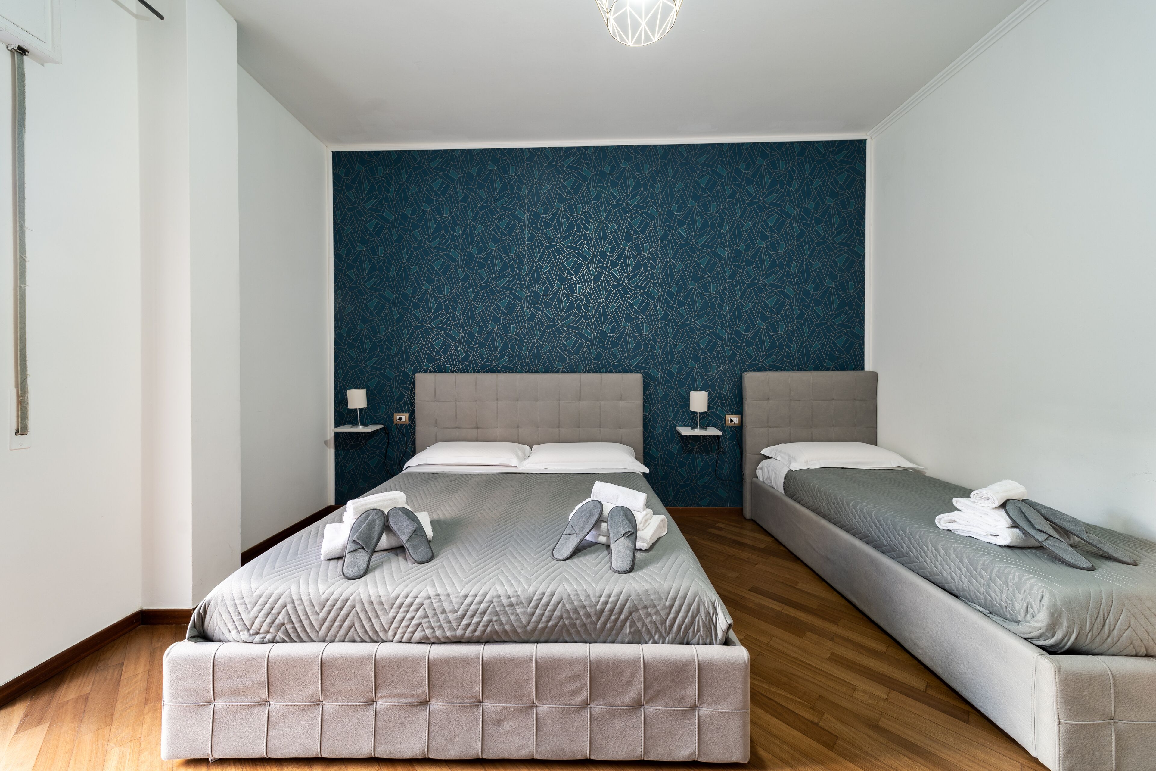 A modern hotel room with a large bed, two bedside tables, and a blue patterned wall.
