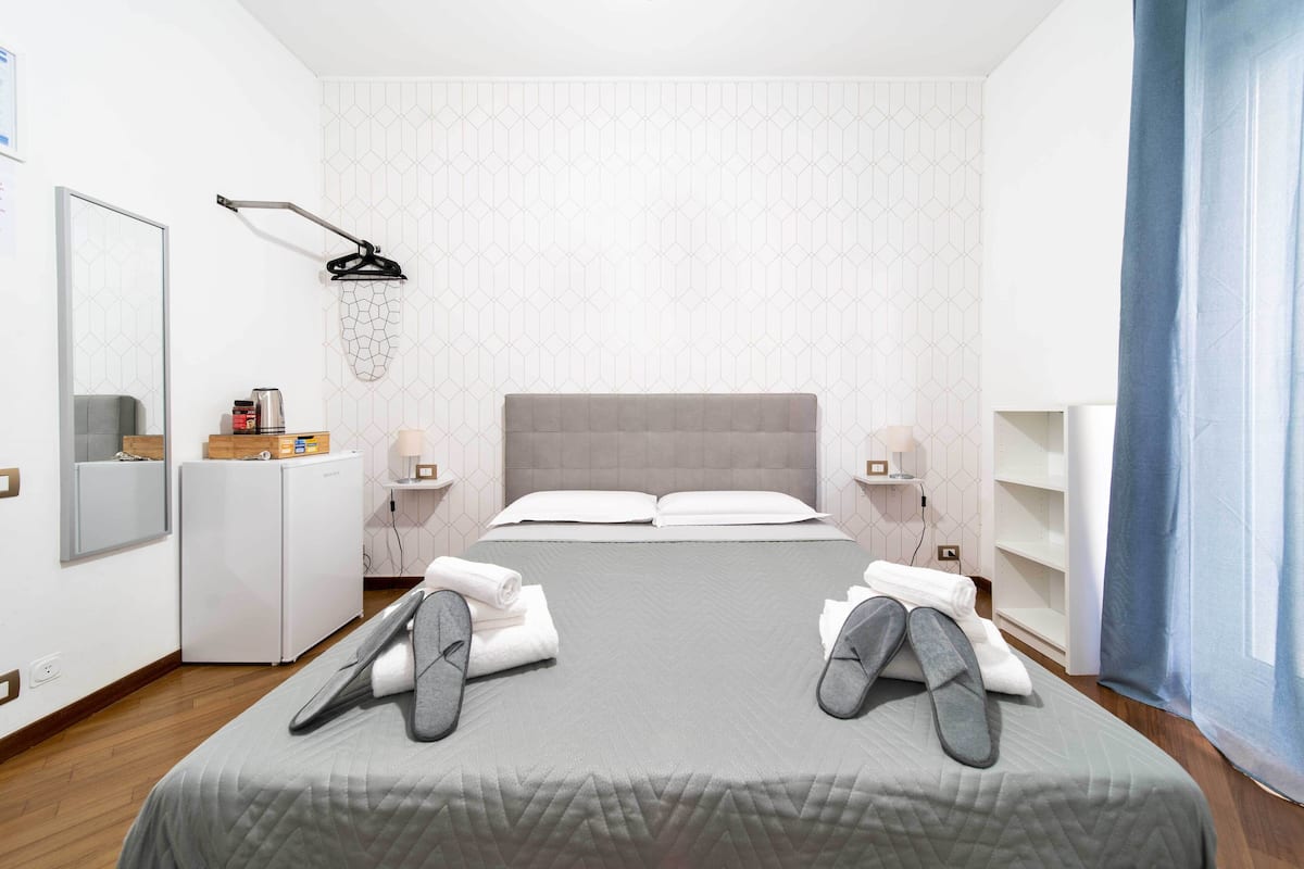 A modern hotel room with a large bed, a desk, a mirror, and a shower.