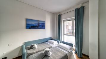 A room with two beds, a painting of a pier, and a window with curtains.