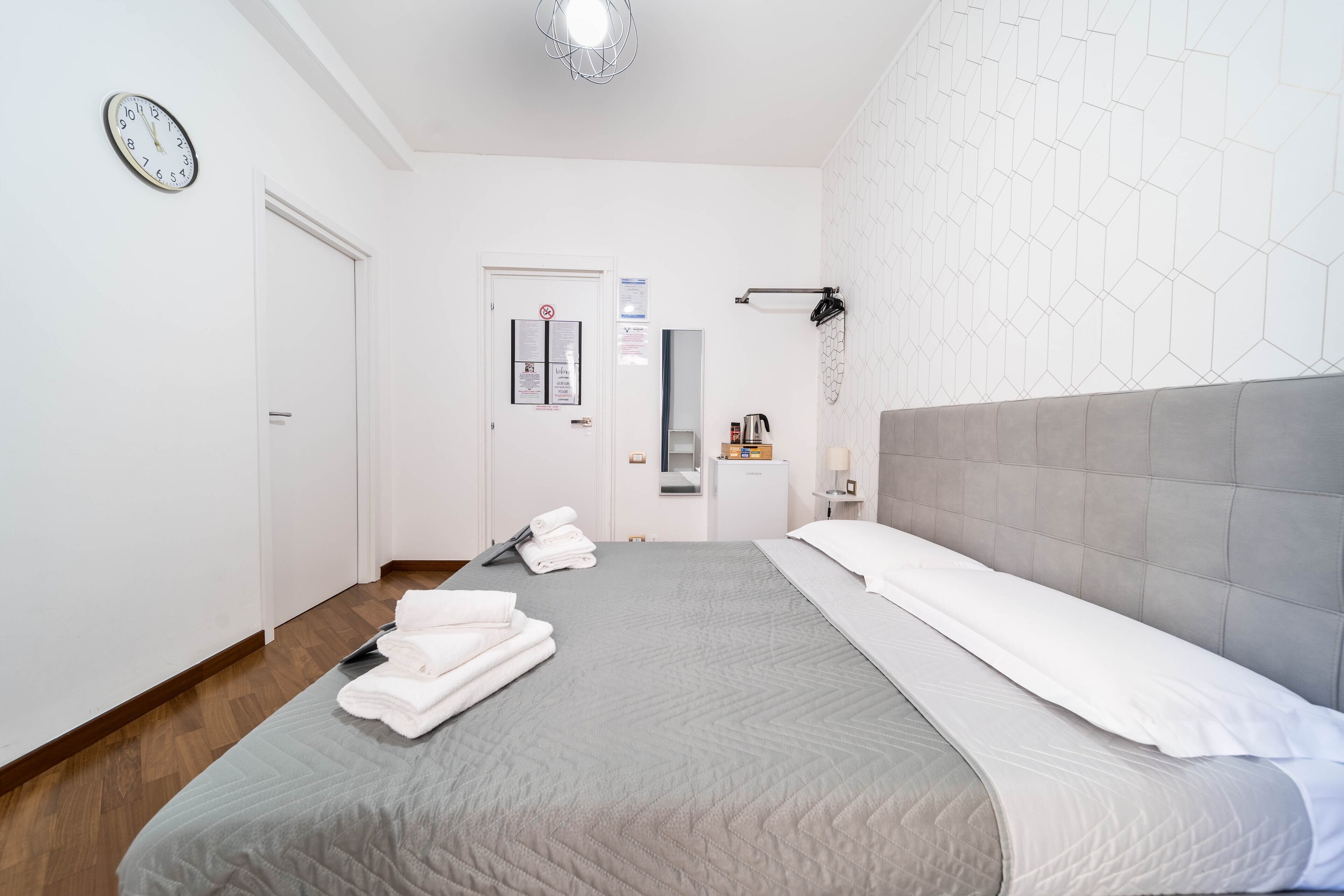 A hotel room with a bed, a clock, a door, and a wall with a geometric pattern.
