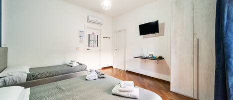 A hotel room with two beds, a TV, a wooden wardrobe, and a mounted shelf.