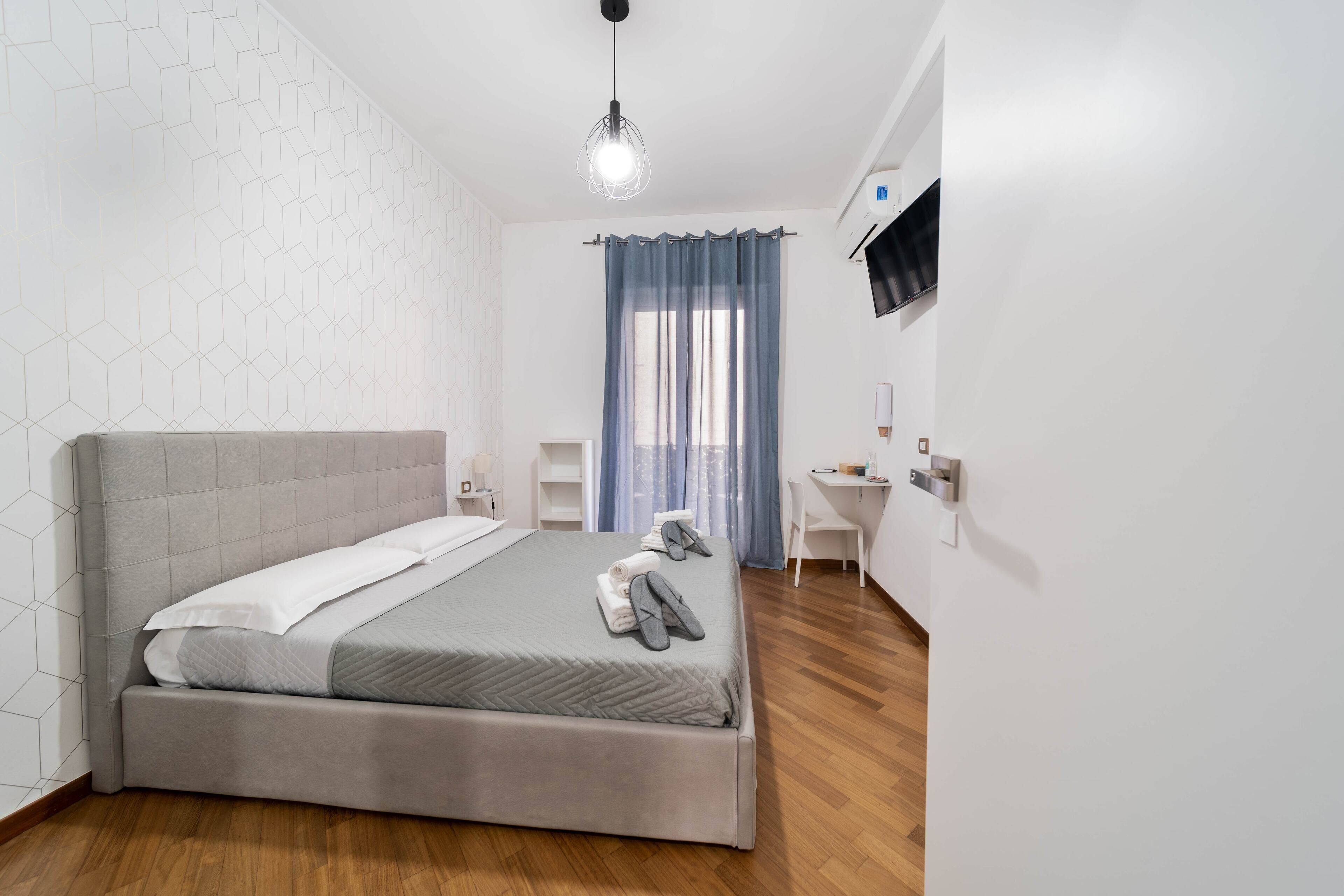 A modern bedroom with a large bed, a desk, and a TV mounted on the wall.