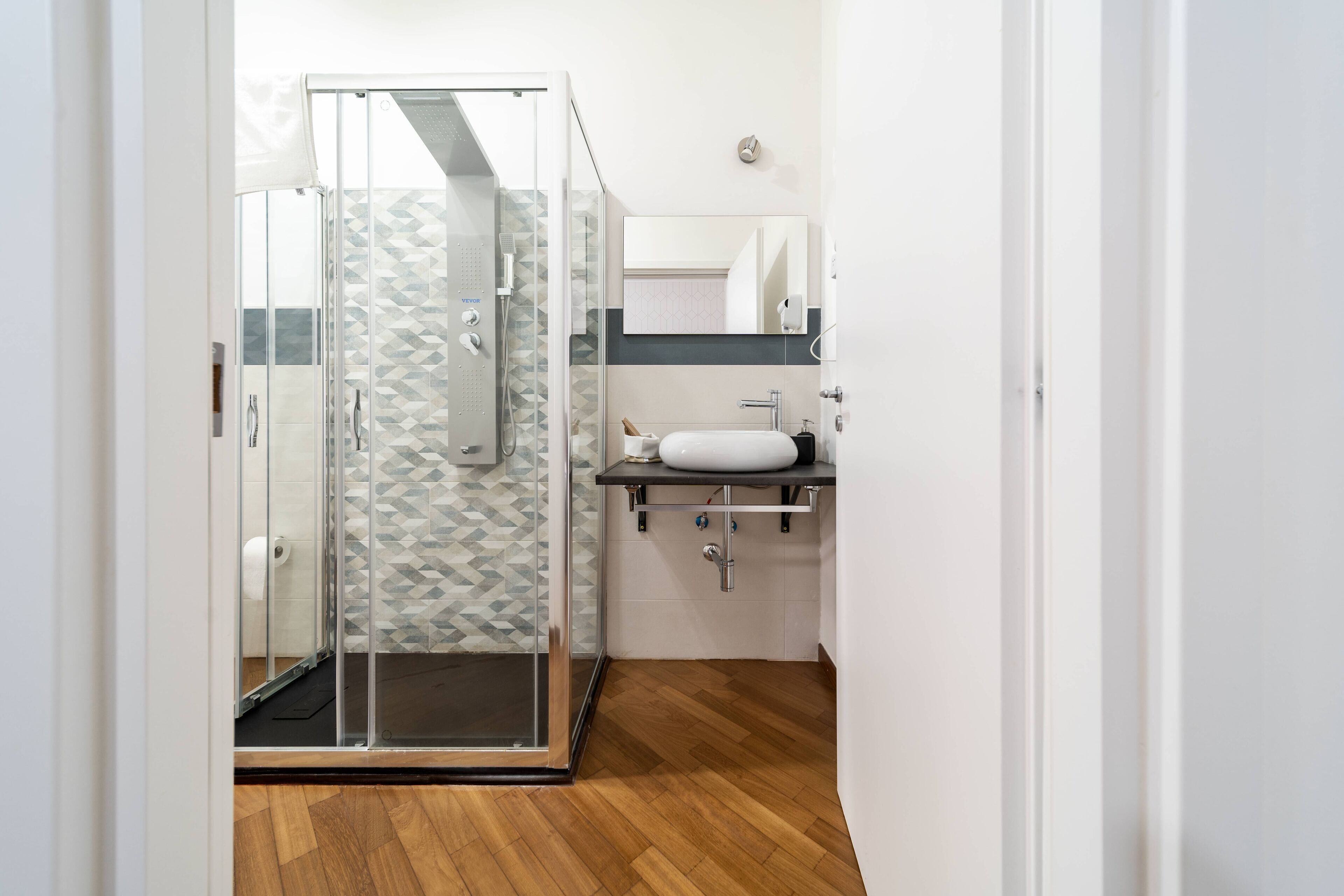 Une salle de bain moderne avec une douche à l’italienne en verre, un lavabo blanc et un plancher en bois.