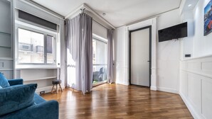 Une pièce spacieuse avec un plancher en bois, un canapé bleu et une grande fenêtre avec des rideaux.