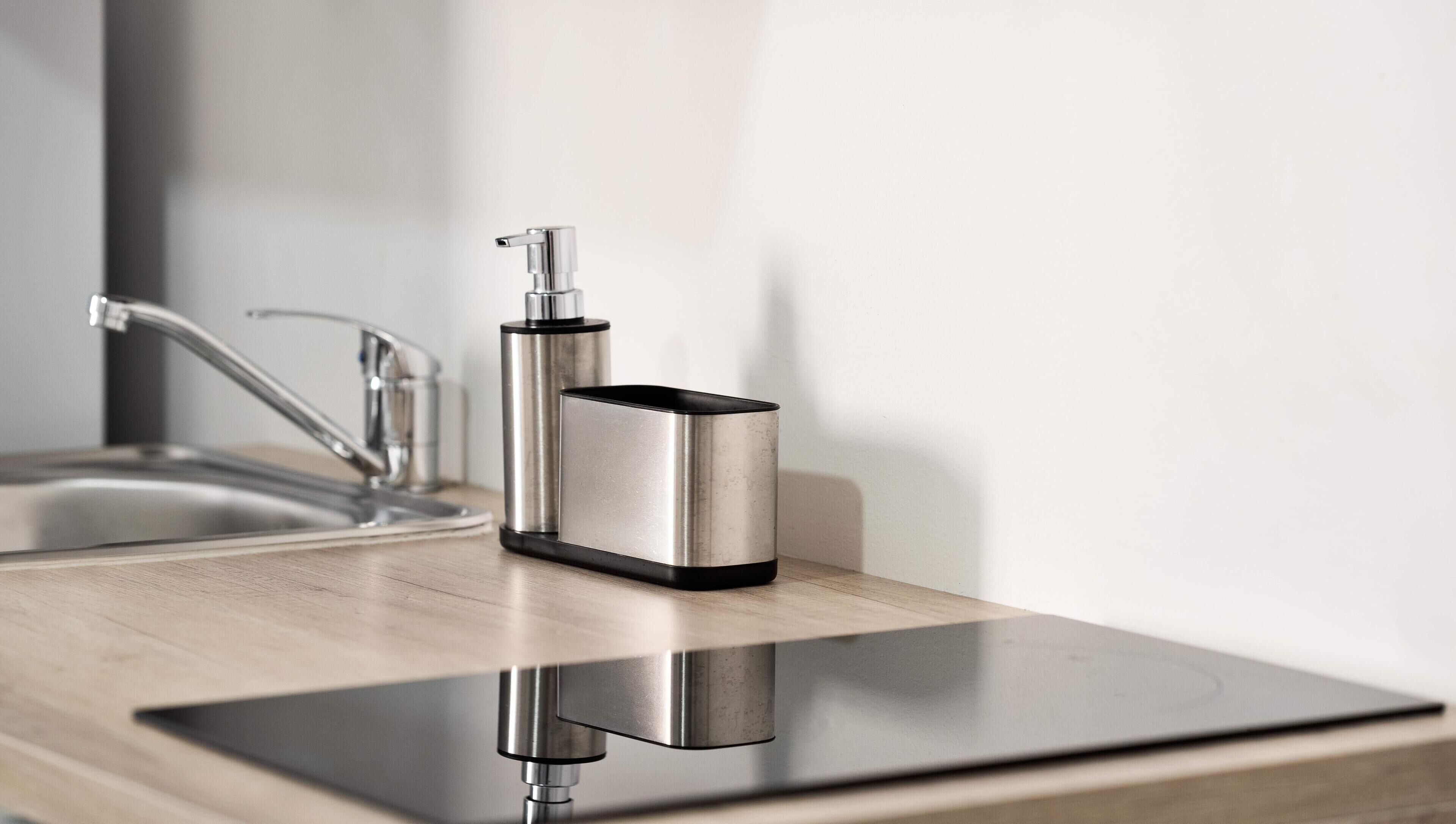 Een moderne badkamer met een roestvrijstalen kraan en een zwarte en zilveren zeepdispenser op een houten aanrecht.