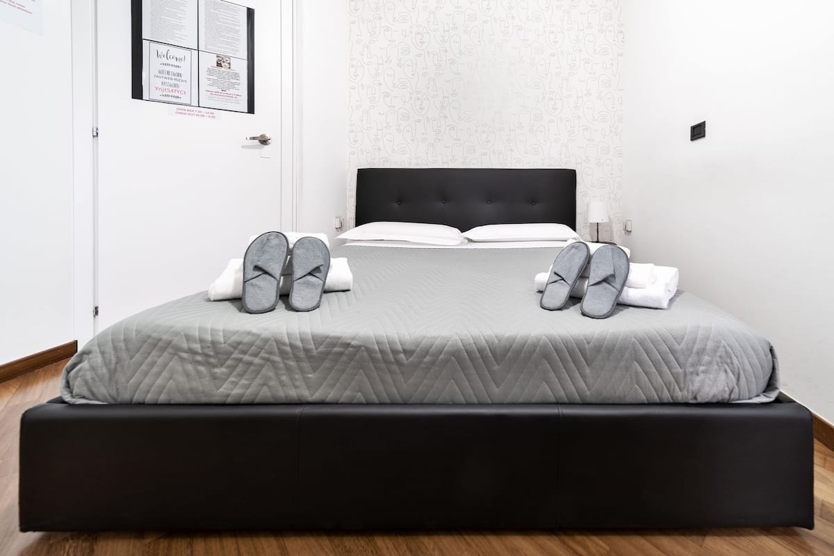 A neatly made bed with a grey quilt, two pillows, and a black headboard.