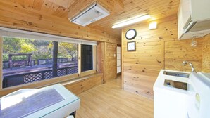 En stuga med träpanel på insidan, ett trägolv, ett fönster med utsikt över en uteplats, ett handfat och en klocka på väggen.
