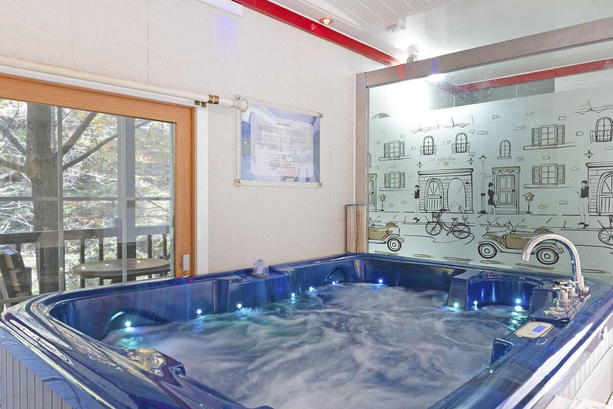 A hot tub with a glass enclosure, a wooden deck outside, and a wall with architectural drawings.