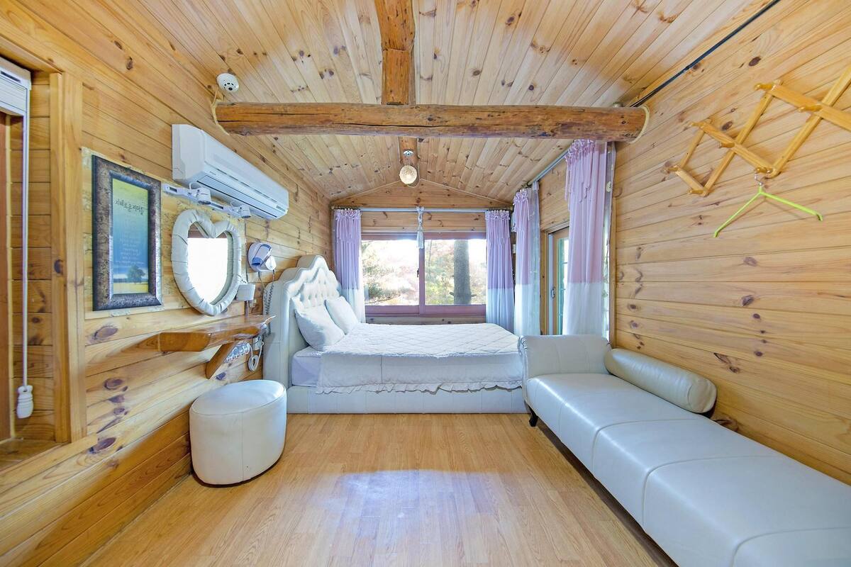 A wooden cabin interior with a bed, a bench, and a small round ottoman.