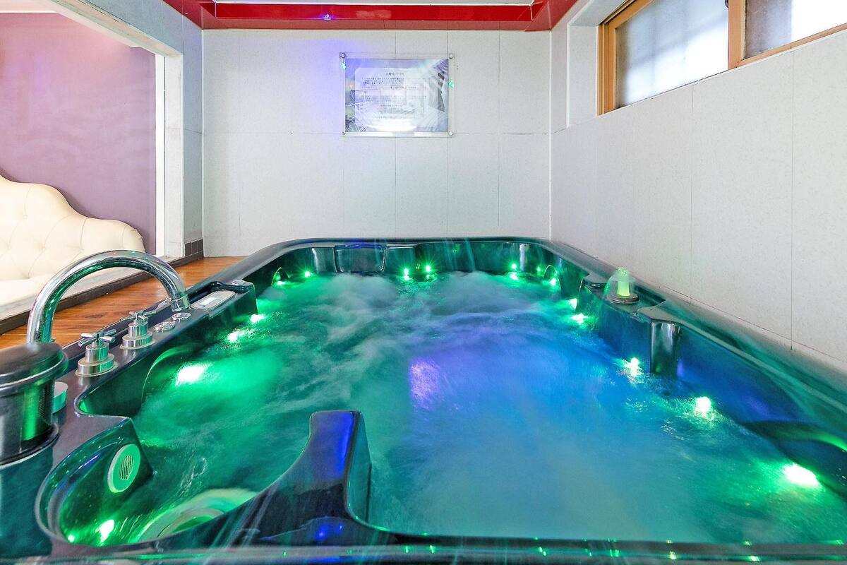 A hot tub with green lighting, a wooden floor, and a white wall with a plaque.