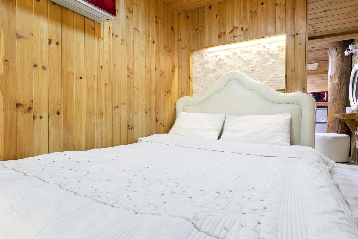 A wooden-paneled room with a bed, a small table, and a mirror.