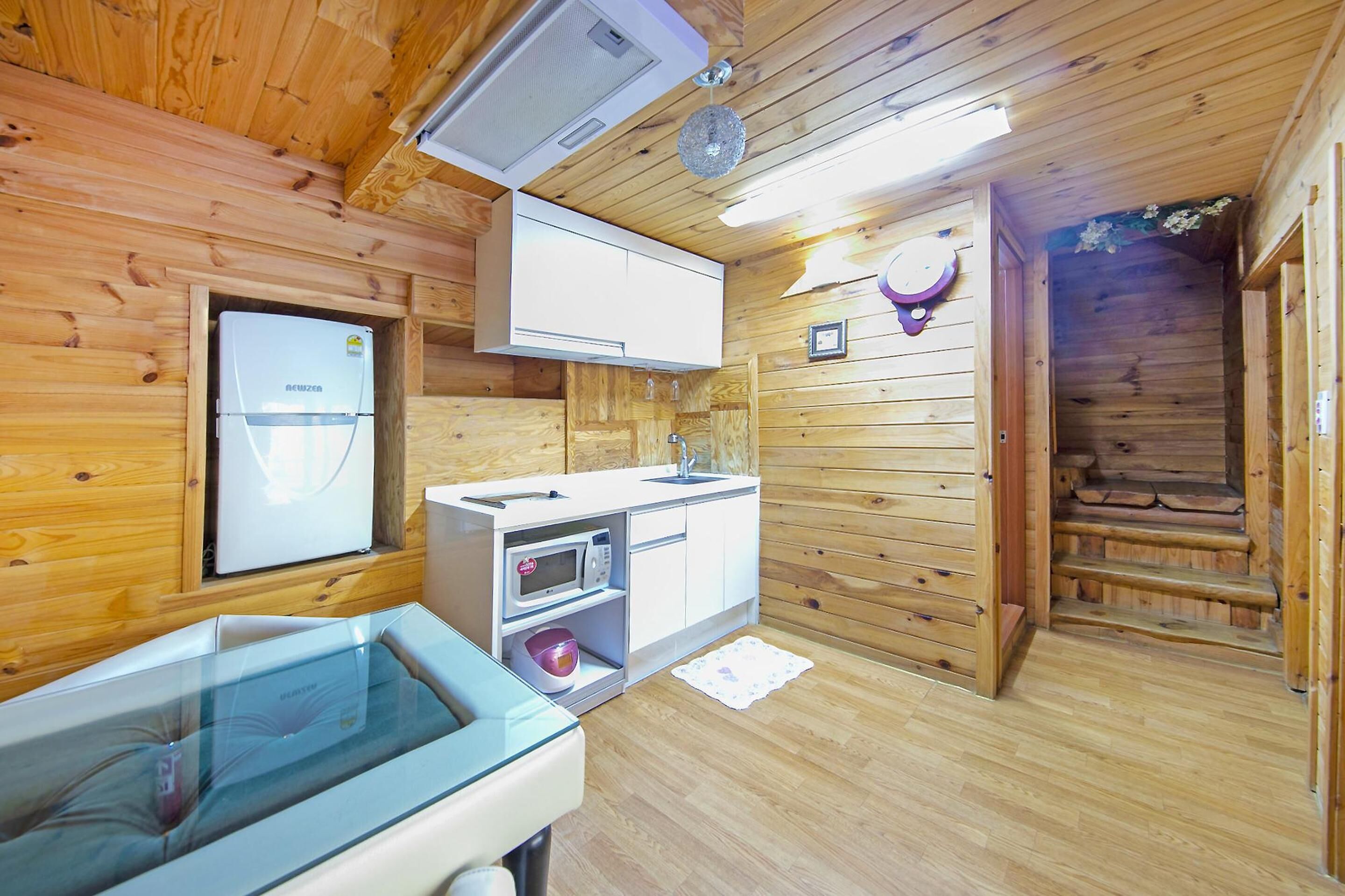 Interior de uma cabana de madeira com cozinha compacta, micro-ondas, geladeira e box de vidro para o chuveiro.