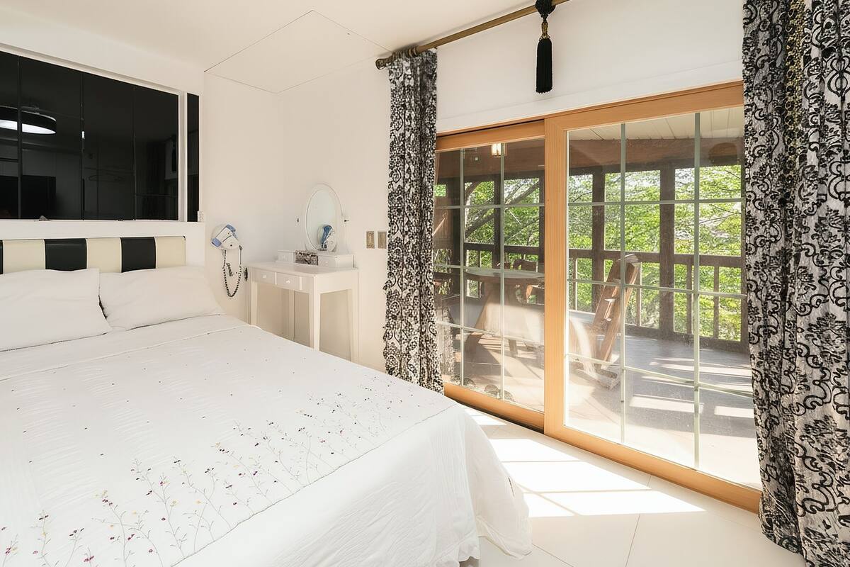 A bedroom with a large bed, a vanity, and a sliding glass door leading to a balcony.