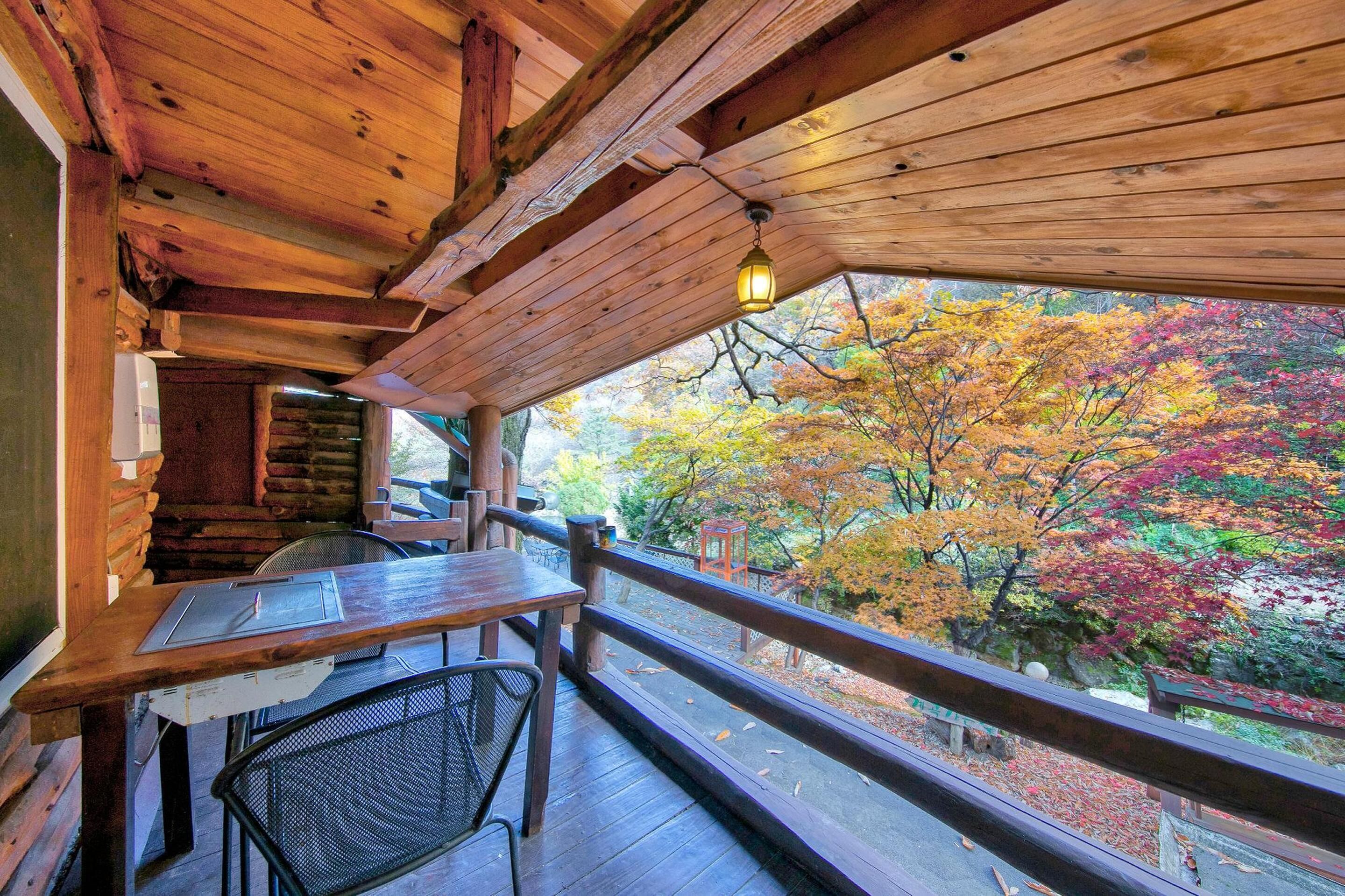 Une terrasse en bois avec une table et des chaises, donnant sur une forêt aux couleurs automnales.