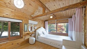 Ett sovrum i en stuga med träpanel, inrett med en säng, en soffa, ett fönster och en taklampa.