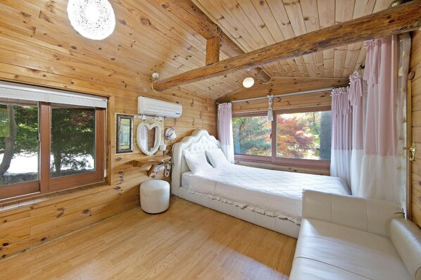 A wooden cabin bedroom with a bed, a sofa, a window, and a ceiling light. - Gapyeong Belita Pension (Gapyeong)