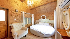 A wooden cabin bedroom with a round bed, a tufted armchair, and a chandelier. - Gapyeong Belita Pension (Gapyeong)