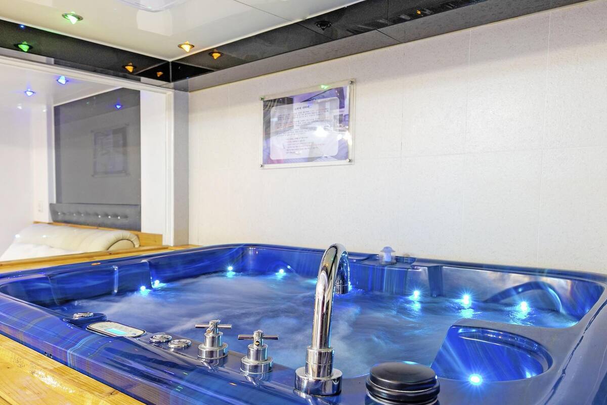 A modern spa room with a large blue hot tub, a wooden bench, and a wall-mounted information board.