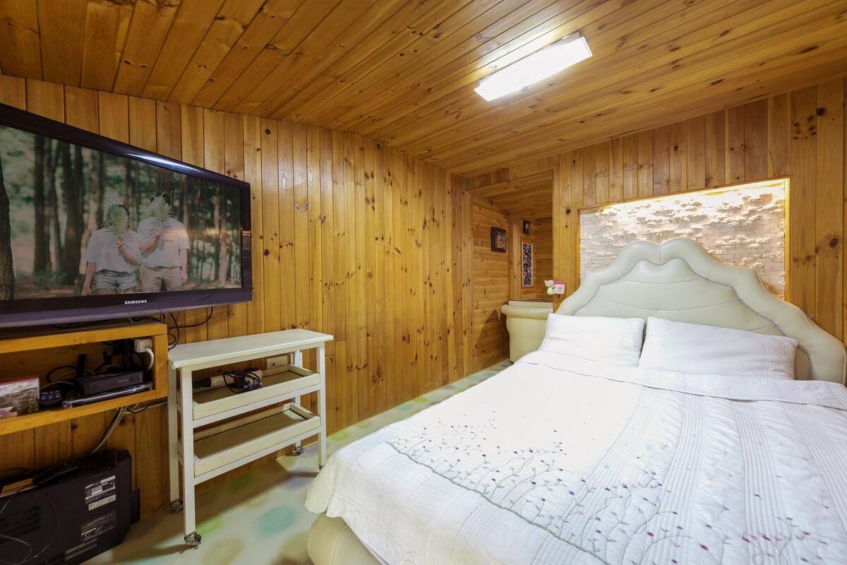 A wooden-paneled room with a bed, a television, and a white headboard.