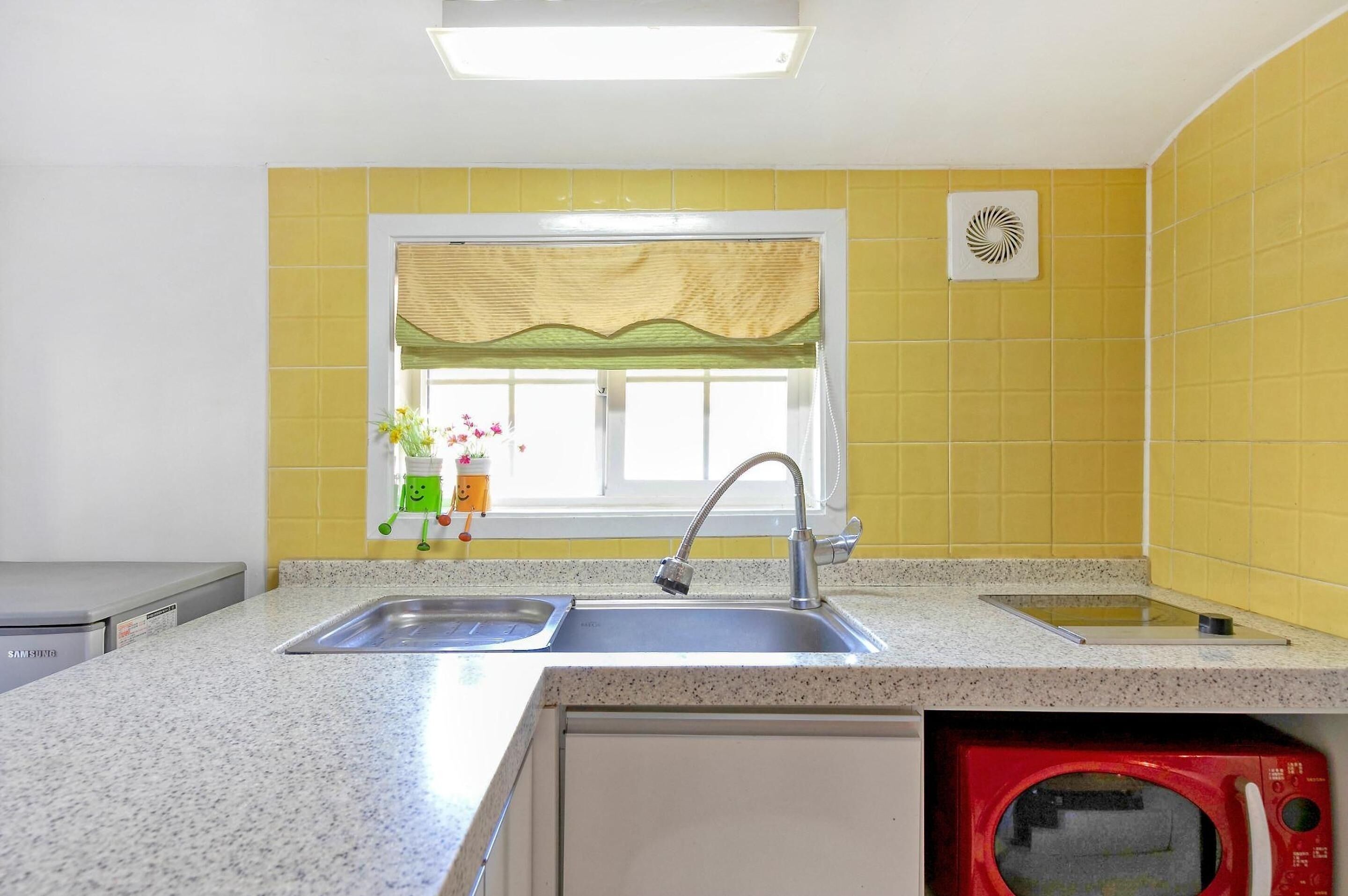 A kitchen with a sink, a window with a green valance, a microwave, and a Samsung refrigerator.