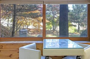 A room with a large window overlooking a forested area. There is a glass-top table and two white chairs. - Gapyeong Belita Pension (Gapyeong)