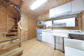 A wooden cabin interior with a kitchen area, wooden staircase, and a white chair. - Gapyeong Belita Pension (Gapyeong)