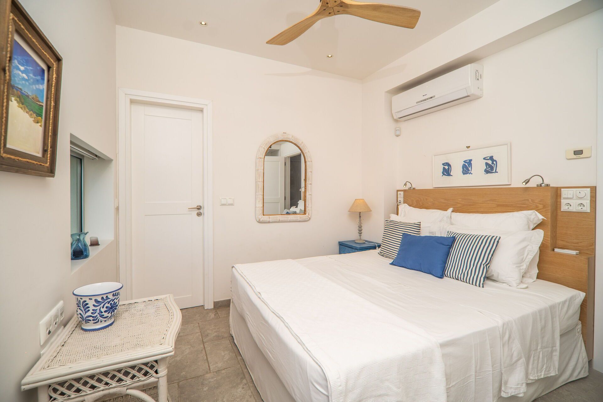 Een slaapkamer met een bed, nachtkastje, spiegel, airconditioning en plafondventilator.