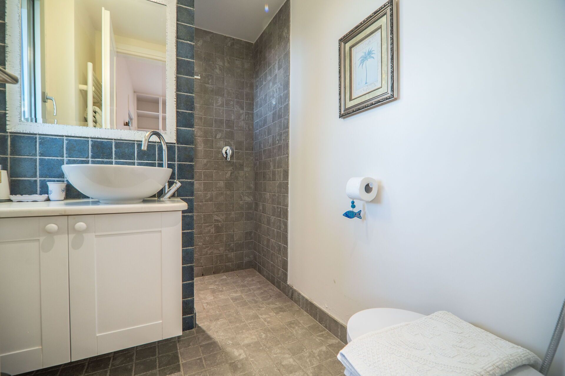 Une salle de bain avec un lavabo blanc, des carreaux bleus, un tableau encadré au mur et des toilettes.
