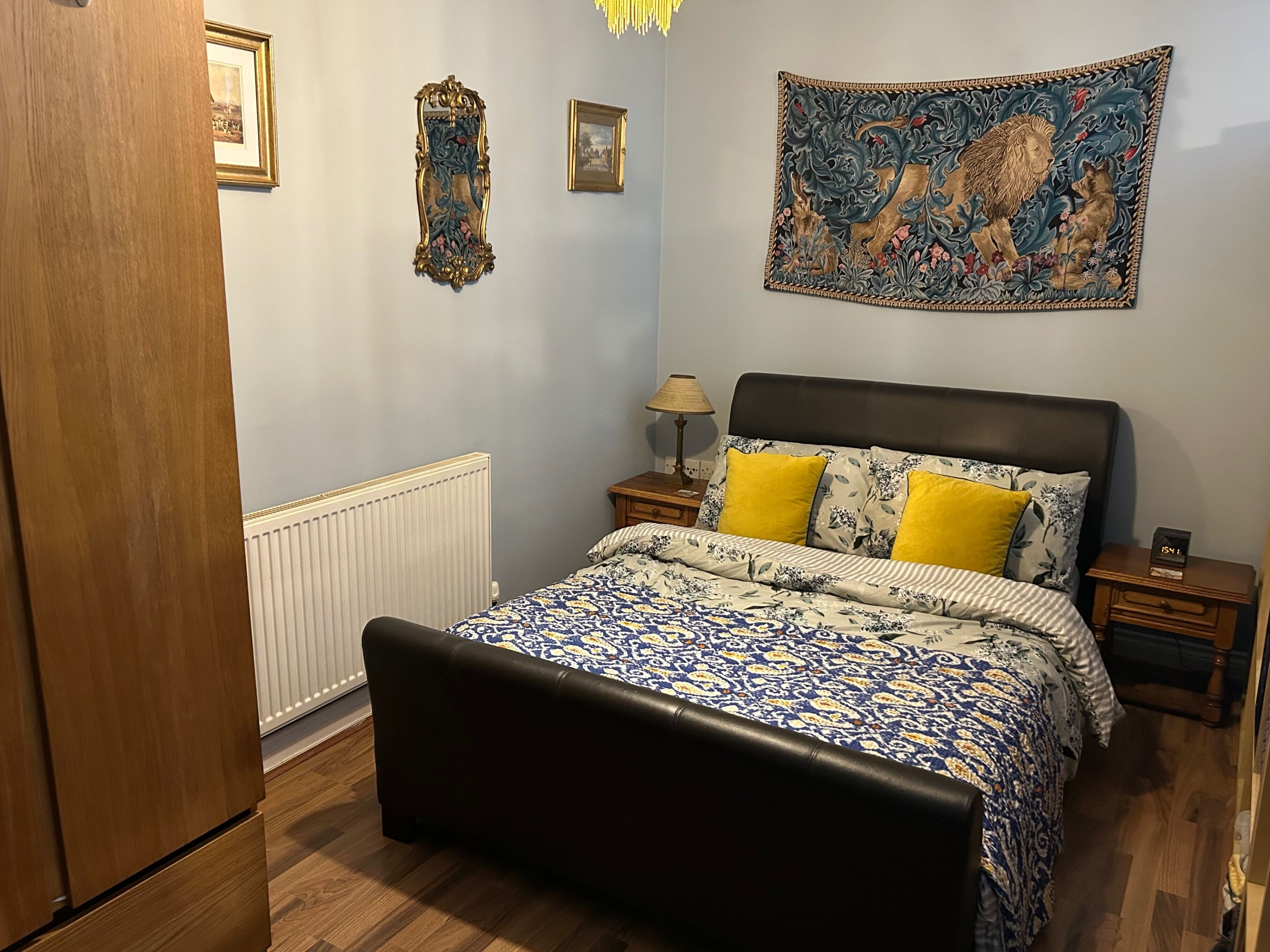 A bedroom with a bed, a nightstand, a lamp, and a tapestry on the wall.