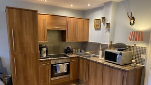 A modern kitchen with wooden cabinets, a built-in oven, a microwave, and a coffee maker. - Beautiful Town Centre Apartment With River Terrace (Macclesfield)