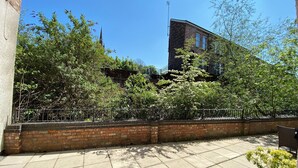 A courtyard with a brick wall, a metal fence, and a building in the background. - Beautiful Town Centre Apartment With River Terrace (Macclesfield)