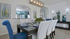 A dining area with a glass-top table, white upholstered chairs, and a modern chandelier. - Luxurious home 2 miles from  Disney - Windsor Hills Resort (Kissimmee)