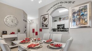 Comedor con una mesa dispuesta para cuatro, sillas blancas y un reloj en la pared.