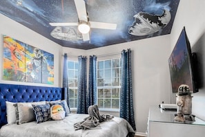 A bedroom with a tufted headboard, a bed with pillows, a ceiling fan, and Star Wars-themed artwork.