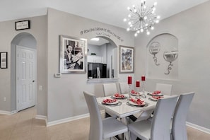 A dining area with a white table set for four, red candles, and framed pictures on the wall.