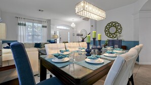 A dining area with a wooden table set for four, blue upholstered chairs, and a chandelier above. - Luxurious home 2 miles from Disney - Windsor Hills Resort (Kissimmee)