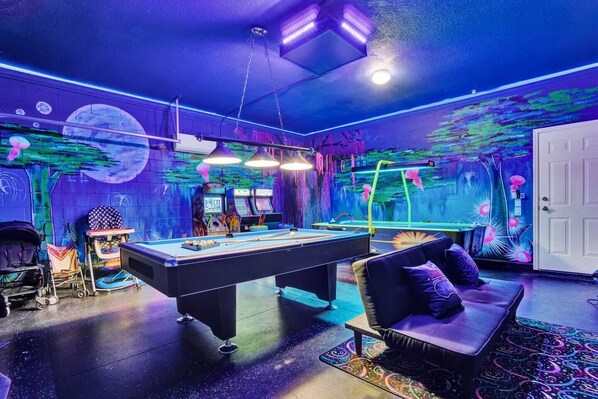 Une pièce équipée d’une table de billard, de jeux d’arcade et ornée d’une fresque représentant une scène de forêt.