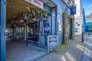 An outdoor seating area of The Fuchsia Coffee Cafe with hanging plants and wicker lamps.