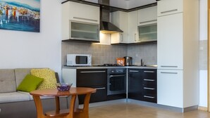 Een kleine keuken met witte kastjes, een magnetron, een fornuis en een eettafeltje.